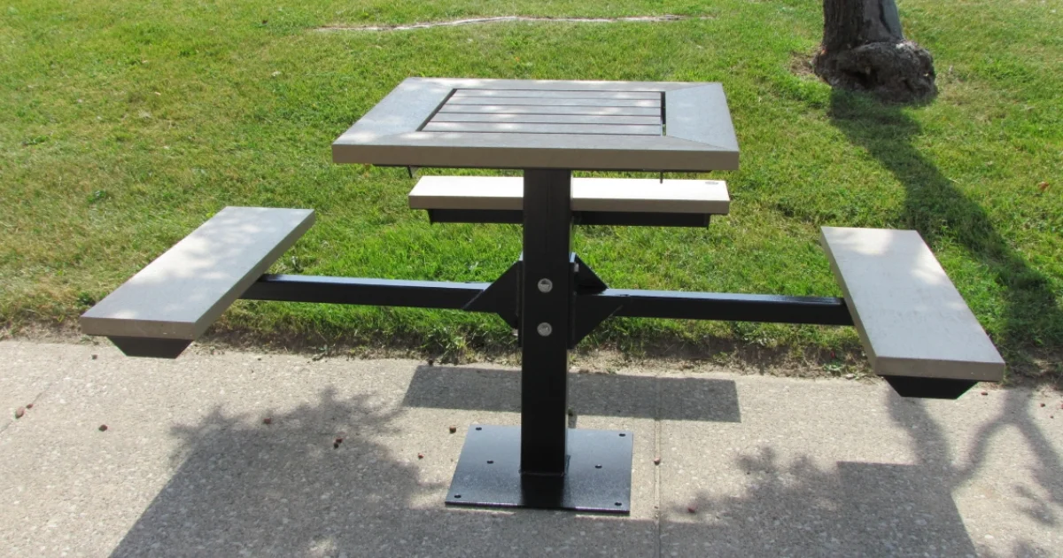 Wheelchair-accessible picnic table with attached benches on a concrete path near grass